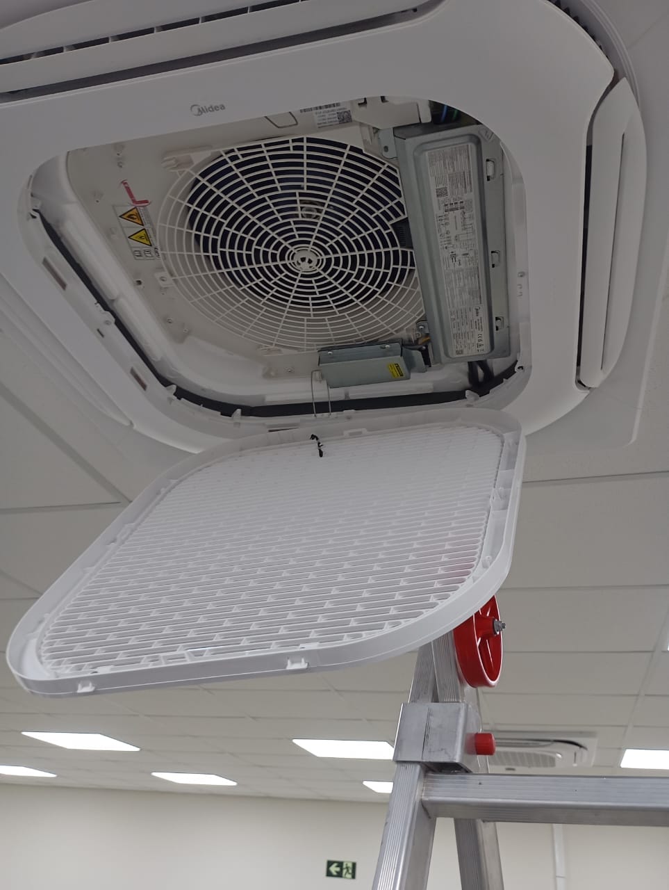 ar-condicionado cassete Midea aberto no teto com o filtro retirado, visto de uma escada