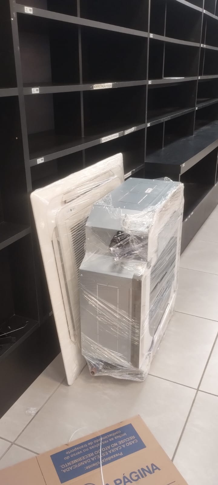aparelhos de ar-condicionado cassete embalados em plástico no chão de uma loja com prateleiras pretas