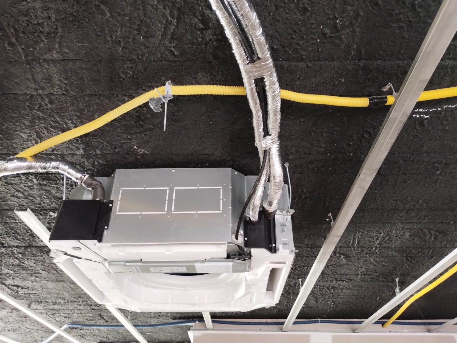 unidade evaporadora de ar-condicionado cassete instalada em teto com estrutura metálica e tubulações revestida
